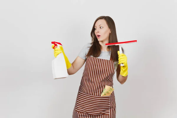 Giovane triste sconvolto casalinga disorientata in guanti gialli grembiule striato pulizia straccio rasoio in tasca isolato su sfondo bianco. Donna mani distese, tenere il flacone spray con liquido detergente. Copia spazio . — Foto Stock