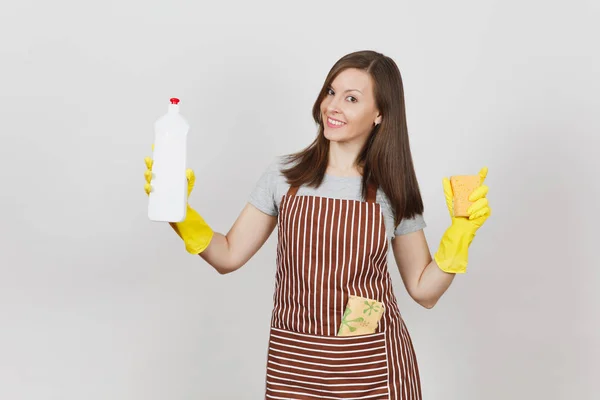 Young housewife in yellow gloves, striped apron, cleaning rag in pocket isolated on white background. Woman spreading hands, holding bottle with cleaner liquid, sponge. Copy space for advertisement. — Stock Photo, Image