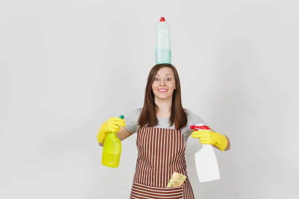 Leuke huisvrouw in gele handschoenen, gestreepte schort, reiniging van rag in zak op witte achtergrond. Vrouw bedrijf in handen, op hoofd flessen met schonere vloeistof voor de afwas. Ruimte voor reclame kopiëren. — Stockfoto