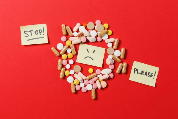 Het kleurrijke ronde tabletten medicatie witte geregeld abstract op rode kleur achtergrond. Aspirine, capsule pillen, papieren sticker vel, tekst stop alstublieft. Triest glimlach gezicht. Beroep, gezonde levensstijl concept. — Stockfoto