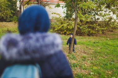 Genç kadın sonbahar park küçük şirin çocuk oğlu ile oynamak, yetişmek, sonbaharda çalıştırın. Anne küçük çocuk evlat gizle ağacın arkasında aramak. Ebeveynlik, Aile günü 15 Mayıs, sevgi, anne, çocuk kavramı.