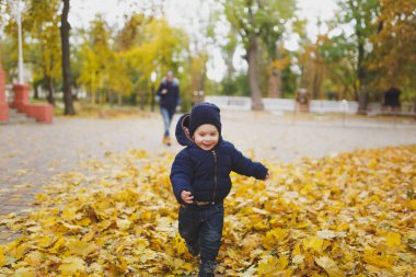Genç kadın walk ın park küçük şirin çocuk oğlu ile düşmek, yetişmek, Kuru sarı sonbahar yaprakları çalıştırın. Anne, küçük bir çocuk evlat dinlenme. Ebeveynlik, Aile günü 15 Mayıs, sevgi, anne, çocuk kavramı