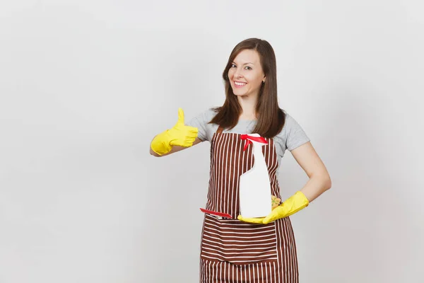 家庭主妇在黄色手套条纹围裙清洗抹布在白色背景的口袋隔离。女管家的妇女显示拇指拿着喷雾瓶与清洁液体。瓶拷贝空间. — 图库照片