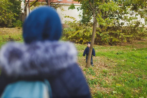 Genç kadın sonbahar park küçük şirin çocuk oğlu ile oynamak, yetişmek, sonbaharda çalıştırın. Anne küçük çocuk evlat gizle ağacın arkasında aramak. Ebeveynlik, Aile günü 15 Mayıs, sevgi, anne, çocuk kavramı.