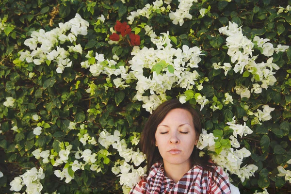 Portret van jonge aantrekkelijke mooi cutie brunette vrouw in warme zonnige zomerdag in groene struiken met witte bloemen voor stenen rock hek. Sensualiteit — Stockfoto