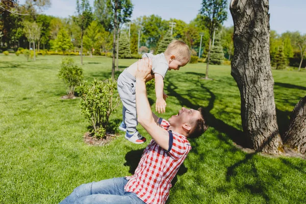 Człowiek radosny spacer na zielony park, reszta, mieć zabawa, gry, wysoki podrzucać do góry małe dziecko cute baby chłopiec siedzieć na trawie w drzewo. Ojciec rzucać synka dziecko. Dzień rodziny 15 maja, miłości rodziców, dzieci koncepcja. — Zdjęcie stockowe