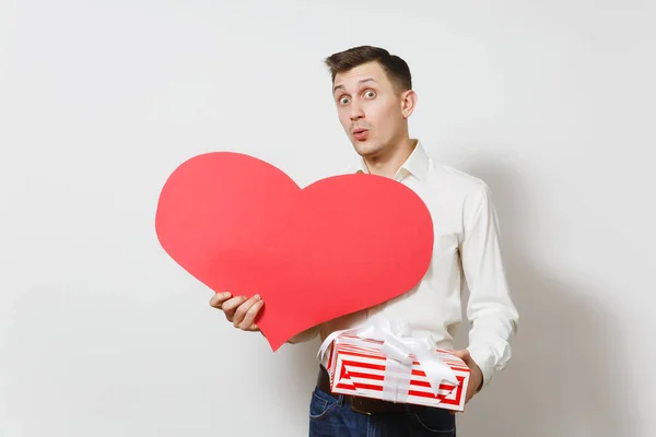 Hombre insatisfecho en camisa sosteniendo gran corazón rojo, presente caja con regalo aislado sobre fondo blanco. Copia espacio para la publicidad. Día de San Valentín, Día Internacional de la Mujer concepto de fiesta de cumpleaños . — Foto de Stock