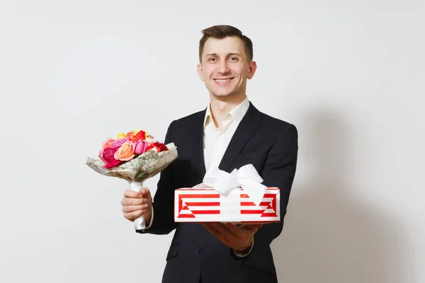 Молодой красивый мужчина в костюме держит букет красивых цветов роз, красный подарок коробку с подарком изолированы на белом фоне. День святого Валентина, концепция празднования Международного женского дня рождения . — стоковое фото