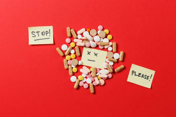Лекарства белые красочные круглые таблетки расположены абстрактно на красном фоне цвета. Аспирин, капсульные таблетки, лист бумаги, текст стоп, пожалуйста. Грустная улыбка. Обращение, концепция здорового образа жизни . — стоковое фото