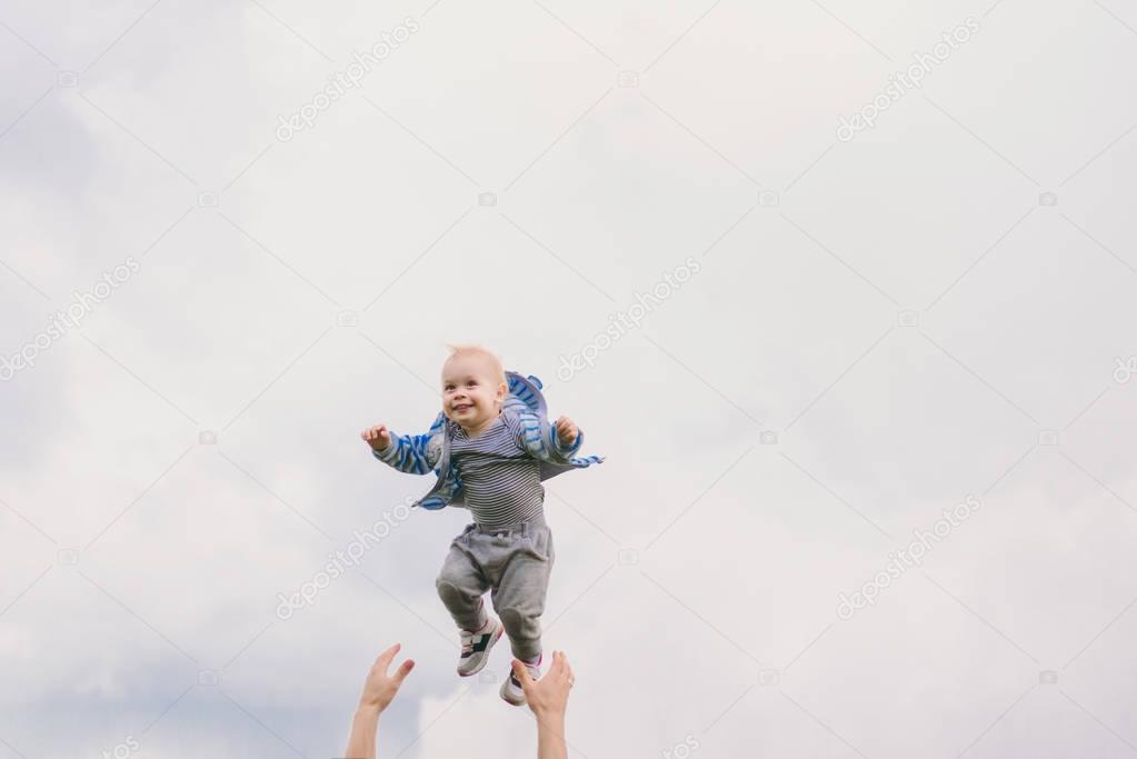 Man hands high toss up little cute child baby boy on blue clouds sky background. Father rest, have fun, play, throw up little kid son. Family day 15 of may, love, parents, children concept.