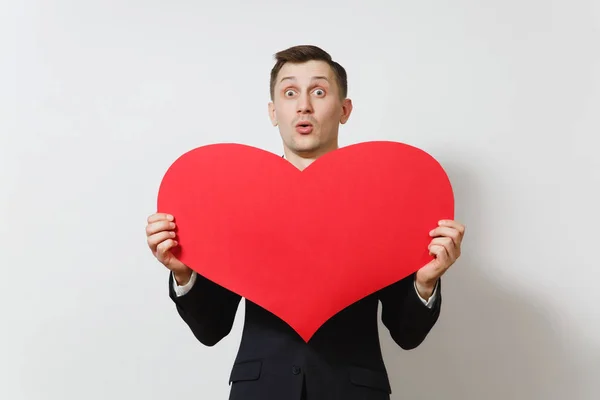 Young stunned shocked upset sad man in suit holding big red heart isolated on white background. Copy space for advertisement. St. Valentine's Day, International Women's Day, birthday, holiday concept. — Stock Photo, Image