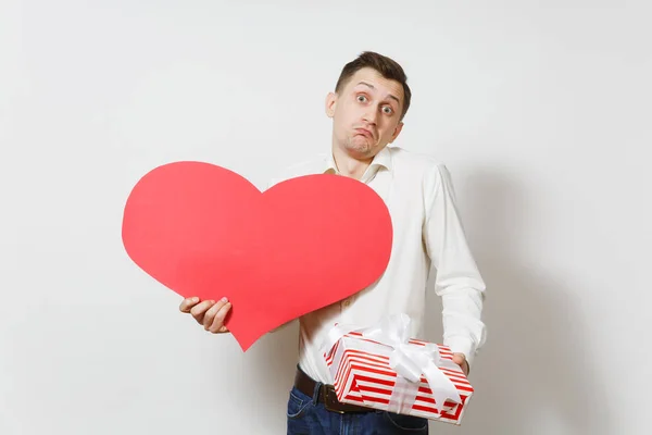 Nespokojený muž v košili drží velké červené srdce, představují pole s darem izolovaných na bílém pozadí. Kopírovat prostor pro reklamu. Svatého Valentýna, Mezinárodní den žen narozeniny svátek koncept. — Stock fotografie