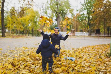 Genç kadın küçük şirin çocuk oğlu, tura atmak kadar kuru sarı sonbahar yaprakları ile sonbahar Parkta yürümek. Anne, küçük bir çocuk evlat dinlenme. Ebeveynlik, Aile günü 15 Mayıs, sevgi, anne, çocuk kavramı.