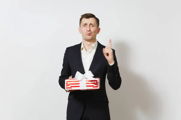 Man in suit pointing index finger up holding red present box with gift isolated on white background. Copy space for advertisement. St. Valentines Day International Women\'s Day birthday holiday concept