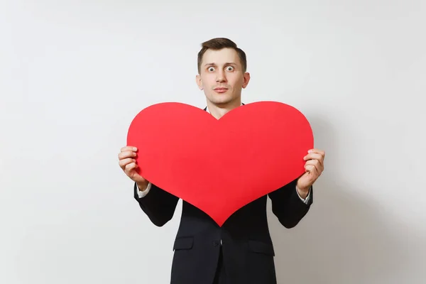 Joven sorprendido sorprendido molesto triste hombre en traje sosteniendo gran corazón rojo aislado sobre fondo blanco. Copia espacio para la publicidad. Día de San Valentín, Día Internacional de la Mujer, cumpleaños, concepto de fiesta . — Foto de Stock