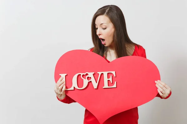 Effektive junge lächelnde Frau in roter Freizeitkleidung mit großem roten Herz, hölzernem Wort Liebe auf weißem Hintergrund. Kopierfläche für Werbung. St. Valentinstag oder Internationaler Frauentag. — Stockfoto