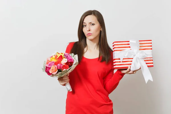Sad upset woman in red clothes holding bouquet of beautiful roses flowers, present box with gift isolated on white background. St. Valentine\'s Day, International Women\'s Day birthday holiday concept.