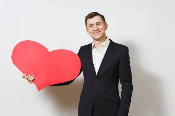 Junger gutaussehender Mann im Anzug, der ein großes rotes Herz auf weißem Hintergrund trägt. Kopierraum, Werbung. Platz für Text. st. valentinstag, internationaler frauentag, geburtstag, ferienkonzept. — Stockfoto