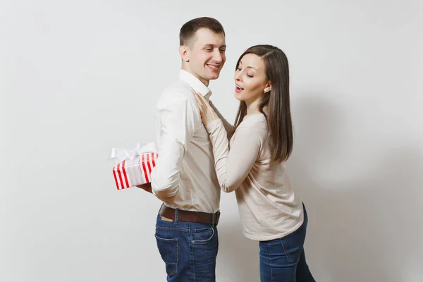 Linda pareja divertida enamorada. Mujer mirando detrás del hombre que se esconde detrás de él caja de regalo rojo con regalo aislado sobre fondo blanco. Día de San Valentín, Día Internacional de la Mujer concepto de fiesta de cumpleaños —  Fotos de Stock