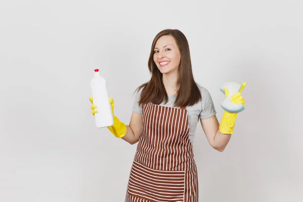 Young smiling housewife in yellow gloves, striped apron isolated on white background. Attractive woman holding bottle with cleaner liquid for washing and cleaning, sponge. Copy space for advertisement — Stock Photo, Image