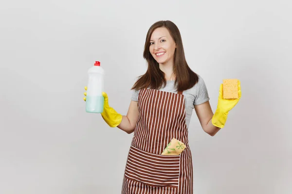 Молода домогосподарка в жовтих рукавичках, смугастий фартух, чистка ганчірки в кишені ізольована на білому тлі. Жінка тримає пляшку з чистою рідиною для миття посуду, губки. Копіювати простір для реклами . — стокове фото