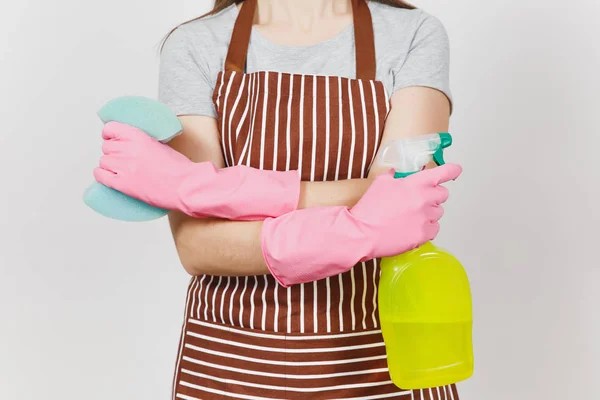 Close up cropped portrait housewife in pink gloves, striped apron isolated on white background. Woman holding hands crossed, spray bottle with cleaner liquid, sponge. Copy space for advertisement. — Stock Photo, Image