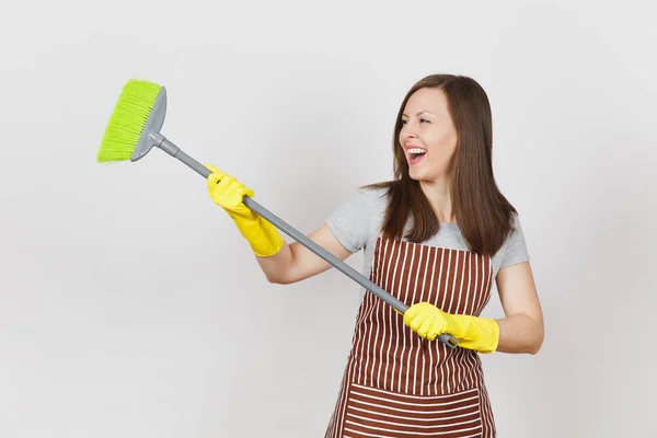 Jovem dona de casa sorridente em avental listrado, luvas amarelas isoladas em fundo branco. Diversão dona de casa mulher limpeza empregada segurando e varrendo com vassoura. Espaço de cópia para área de publicidade — Fotografia de Stock