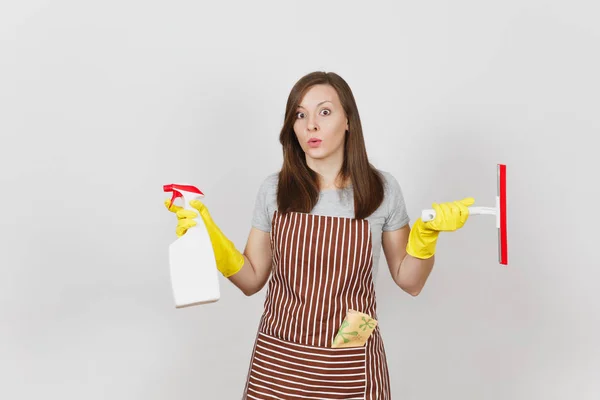 Young sad upset bewildered housewife in yellow gloves striped apron cleaning rag squeegee in pocket isolated on white background. Woman spread hands, hold spray bottle with cleaner liquid. Copy space. — Stock Photo, Image