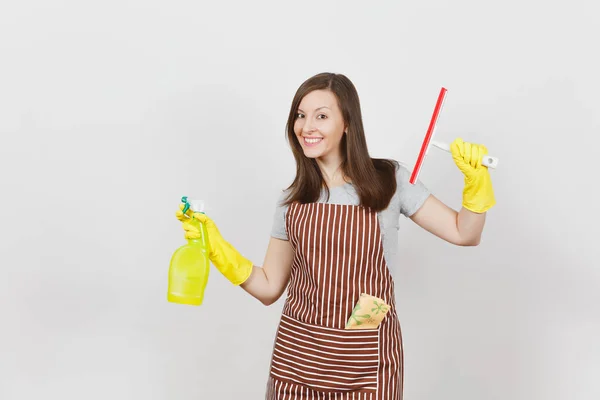 Young smiling housewife in yellow gloves, striped apron, cleaning rag in pocket isolated on white background. Housekeeper woman holding squeegee, spray bottle with cleaner liquid. Bottle copy space. — Stock Photo, Image