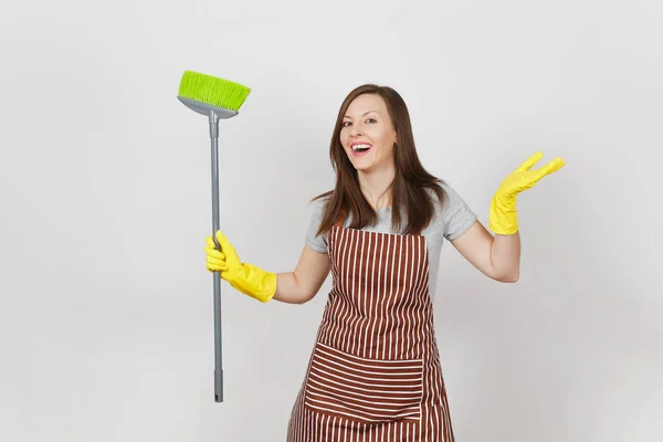 年轻的微笑的主妇在条纹围裙, 黄色手套被隔绝在白色背景。女管家清洁工拿着扫帚清扫女仆。广告广告区域复制空间 — 图库照片