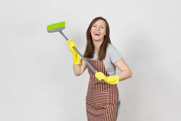 Jonge lachende huisvrouw in gestreepte schort, gele handschoenen geïsoleerd op een witte achtergrond. Leuk huishoudster vrouw schoonmaak meid houden en vegen met bezem. Ruimte voor reclame reclame gebied kopiëren — Stockfoto