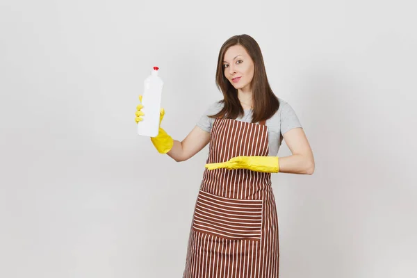 Young housewife in yellow gloves, striped apron isolated on white background. Woman holding and pointing hand on bottle with cleaner liquid for washing and cleaning. Copy space for advertisement. — Stock Photo, Image