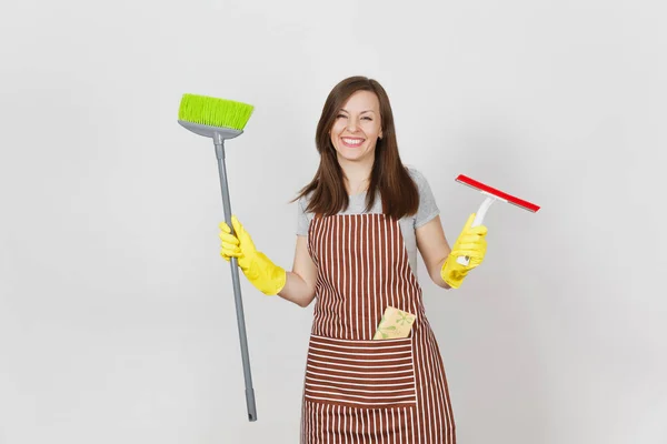 年轻的微笑的主妇在条纹围裙, 黄色手套被隔绝在白色背景。女管家清洁女仆手持, 扫扫帚, 刮胶。为广告复制空间。广告专区. — 图库照片