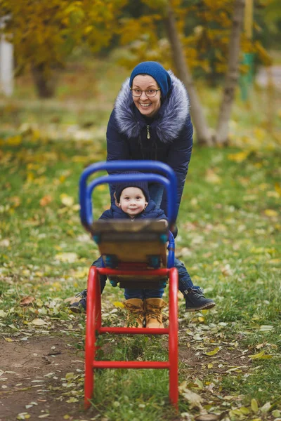 Genç kadın doğa üzerinde küçük şirin çocuk oğlu ile yeşil sarı sonbahar sonbahar Parkta yürümek. Anne, çocuk evlat eğlenceli tutun, salıncağa binmek. Ebeveynlik, Aile günü 15 Mayıs, sevgi, anne, çocuk kavramı. — Stok fotoğraf