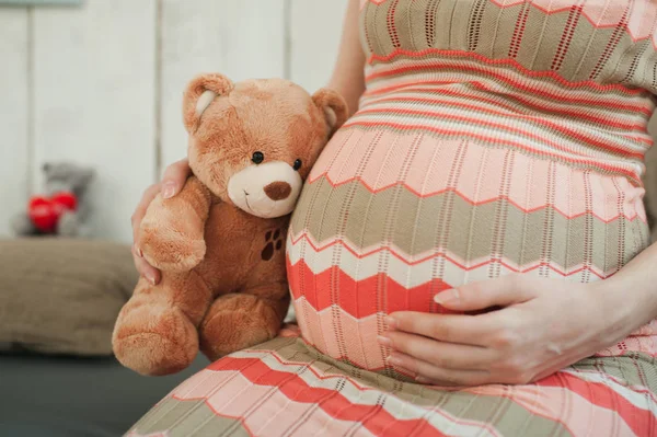 Close up cropped portrait pregnant happy woman in striped long dress with big belly, teddy bear. Tummy toy. Pregnancy, parenthood, family, motherhood, parents, children, people and expectation concept — Stock Photo, Image