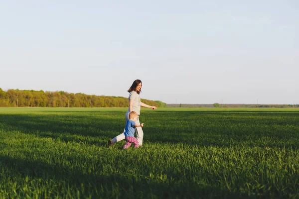 Joyful jovem caminhe no fundo de trigo campo de grama verde, descanso, divirta-se, jogar, correr com pequeno menino bonito criança. Mãe, filho pequeno. Dia de família 15 de maio, amor, pais, conceito de crianças . — Fotografia de Stock