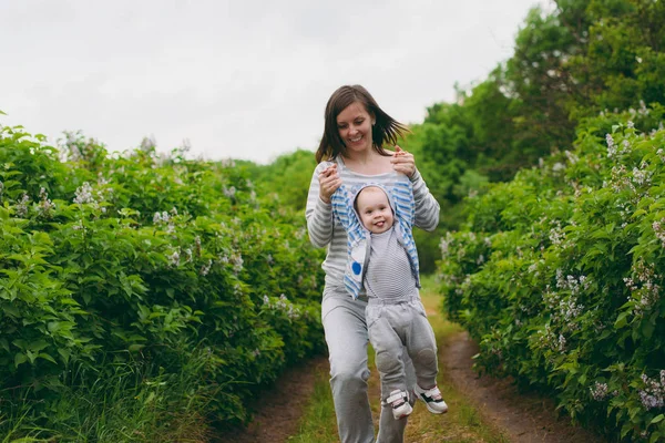 Jovem mulher alegre andando sobre o fundo do parque da natureza segurando as mãos, circulando pequeno menino bonito criança. Mãe, filhinho. Paternidade, dia de família 15 de maio, amor, pais, conceito de crianças . — Fotografia de Stock