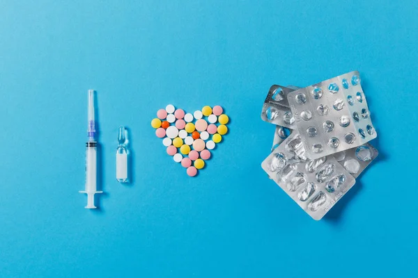 Medicatie wit, kleurrijke ronde tabletten in vorm van hart geïsoleerd op blauwe achtergrond. Pillen, verpakkingen, lege spuit-naald. Concept van behandeling, keuze, gezonde levensstijl. Ruimte reclame kopiëren. — Stockfoto