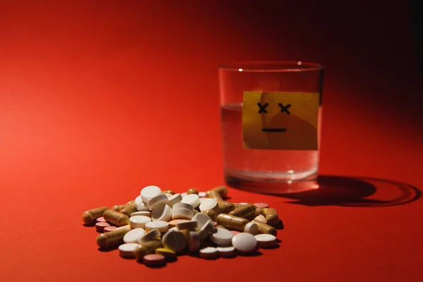 Лекарства белые красочные таблетки таблетки расположены абстрактно на темно-красном фоне цвета. Конструкция капсулы стеклянной воды. Выбор лечения концепции здорового образа жизни. Бумажная наклейка грустная улыбка . — стоковое фото