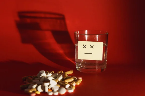 Gyógyszert fehér színes tabletta tabletták rendezett absztrakt a háttér sötét vörös színű. Kapszula üveg pohár víz tervez. Kezelés választás egészséges életmód fogalma. Papír matrica lap szomorú mosollyal arcán. — Stock Fotó