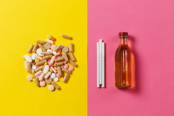 Medicinering färgglada tabletter piller ordnade abstrakt, flaska alkohol, cognac, whisky, tre vita cigaretter på gul rosa ros färgbakgrund. Behandling, val hälsosam livsstil. Kopiera utrymme. — Stockfoto