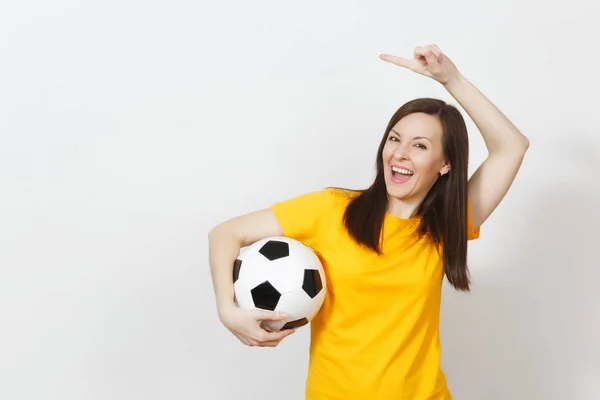 Mujer joven europea, aficionada al fútbol o jugadora de uniforme amarillo sosteniendo la pelota de fútbol señalando con el dedo índice a un lado aislado sobre fondo blanco. Deporte, fútbol, salud, concepto de estilo de vida saludable . — Foto de Stock