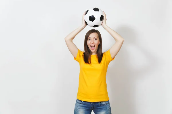 Hermosa joven europea alegre mujer, fanático del fútbol o jugador en uniforme amarillo sosteniendo por encima de la cabeza pelota de fútbol aislado sobre fondo blanco. Deporte, fútbol, salud, concepto de estilo de vida saludable . — Foto de Stock