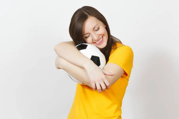 Beautiful European young cheerful happy woman, football fan or player in yellow uniform hugging soccer ball isolated on white background. Sport, play football, health, healthy lifestyle concept.