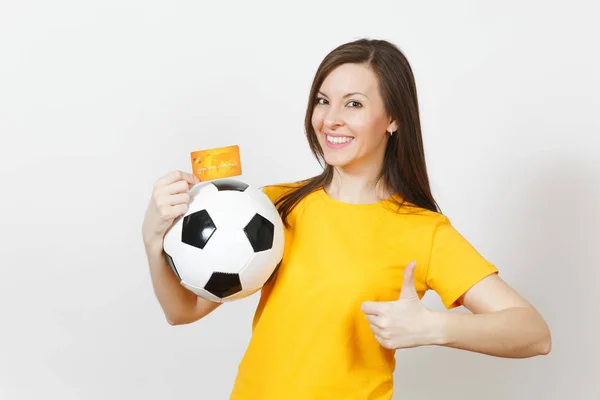 Beautiful European young cheerful woman, football fan or player in yellow uniform holding credit card soccer ball isolated on white background. Sport, play football game, excitement lifestyle concept.