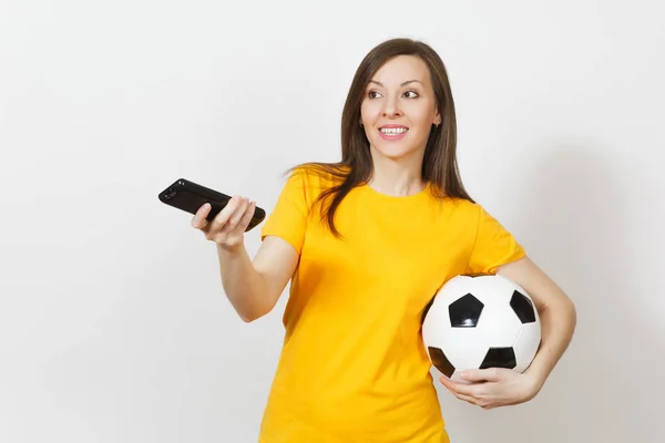 Bella europea giovane donna allegra, tifoso di calcio o giocatore in uniforme gialla tenere telecomando TV, pallone da calcio isolato su sfondo bianco. Sport, calcio, salute, stile di vita sano . — Foto Stock