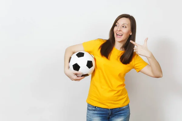 Mujer joven europea, aficionada al fútbol o jugadora de uniforme amarillo sosteniendo la pelota de fútbol señalando con el dedo índice a un lado aislado sobre fondo blanco. Deporte, fútbol, salud, concepto de estilo de vida saludable . — Foto de Stock