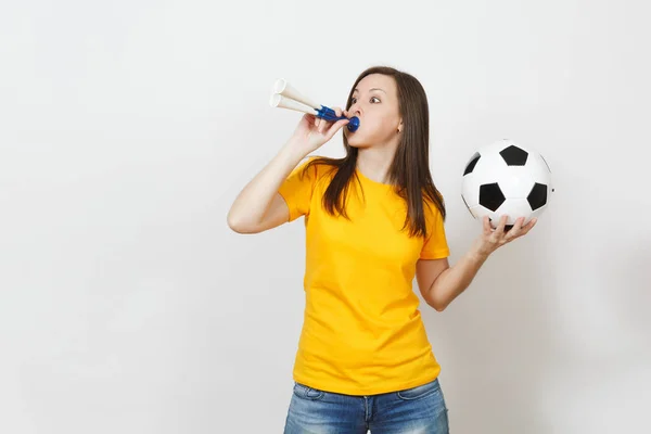 Hermosa joven europea alegre mujer feliz, fanático del fútbol o jugador en uniforme amarillo sostiene y sopla la pipa de fútbol, bola aislada sobre fondo blanco. Deporte, jugar al fútbol, concepto de estilo de vida saludable . — Foto de Stock