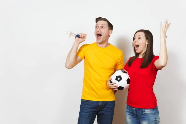 有趣的疯狂欢快的年轻夫妇, 妇女, 男子, 足球球迷在黄色和红色制服振作起来支持队与钢管足球隔离在白色背景。体育, 家庭休闲, 生活方式概念. — 图库照片