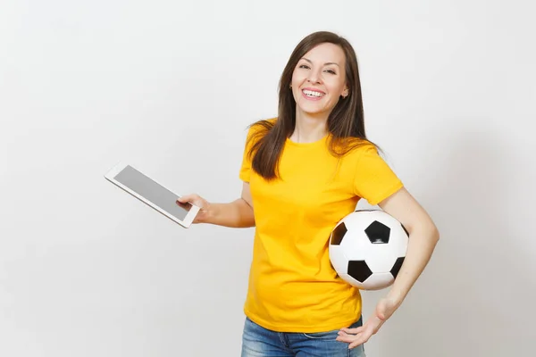 Beautiful European young cheerful woman, football fan or player in yellow uniform holding tablet pc, soccer ball isolated on white background. Sport, play football, health, healthy lifestyle concept.